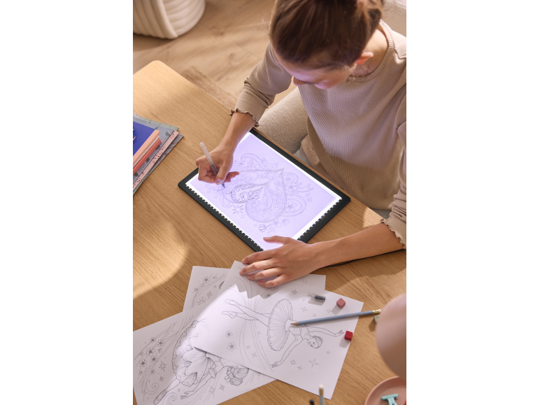 Une fille dessinant sur une table lumineuse LED pour décalquer des dessins.