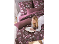 Femme lisant sur un lit avec une housse de couette florale et des oreillers prune unis.