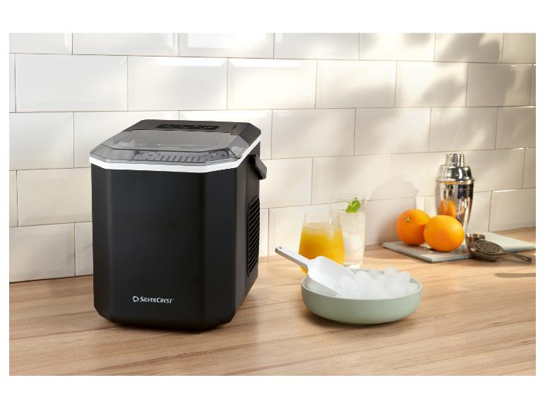 Machine à glaçons noire avec glaçons, boissons et shaker à cocktails sur un comptoir en bois.