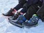 Trois paires de bottes d'hiver noires avec des détails bleus et roses dans la neige.
