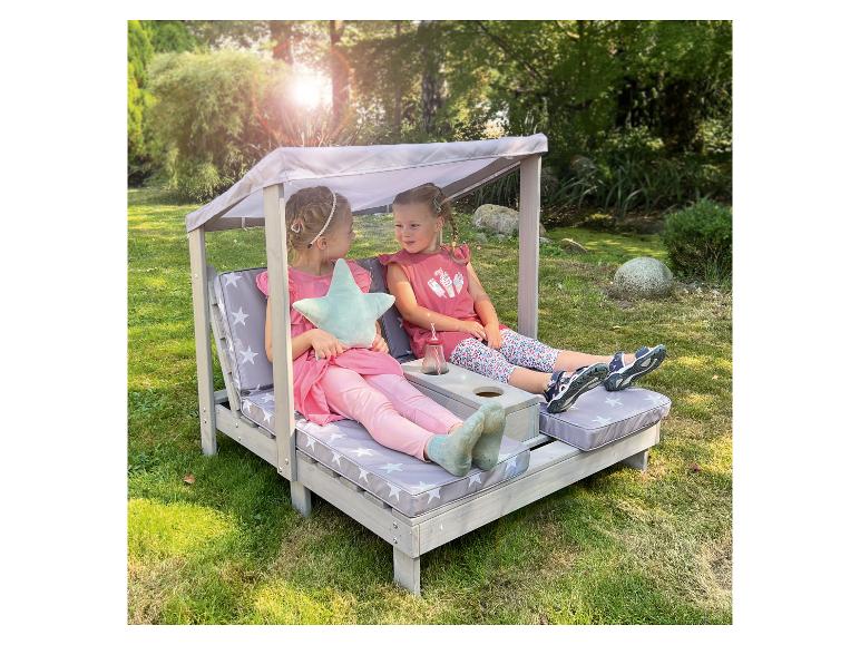 Deux petites filles se détendent sur une banquette de jardin en bois avec des coussins étoilés.