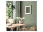 Espace de travail avec bureau, chaise en rotin, papier peint floral vert et plantes suspendues.