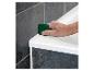 Main lissant le joint de silicone blanc le long d'une baignoire avec un outil vert.