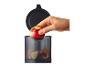 Une main place une pomme rouge dans un robot culinaire noir avec des morceaux de pomme.