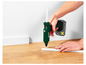 Une personne utilise un pistolet à colle chaude Parkside X20V Team pour fixer une plinthe blanche sur un sol en bois.
