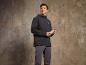 Un homme portant une veste softshell noire et un pantalon gris tient une bouteille d'eau.