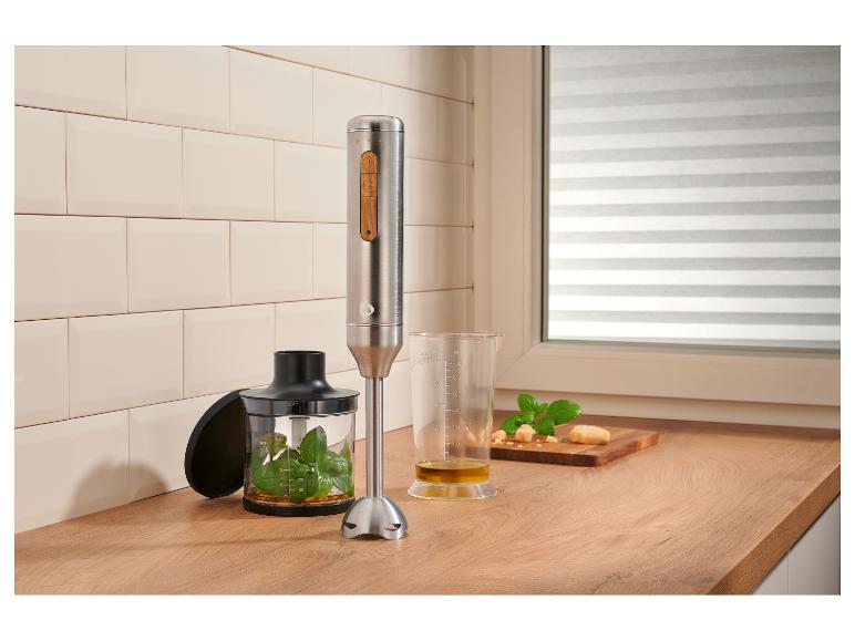 Mixeur plongeant en acier inoxydable avec accents en bois, préparant du pesto sur un comptoir en bois.