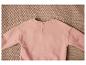 Un pull rose à manches longues avec des boutons sur un fond tricoté.