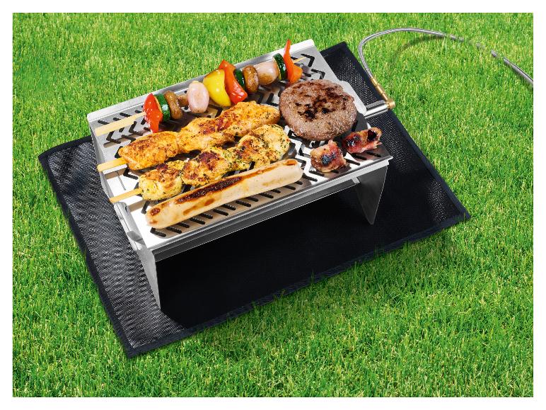 Barbecue à gaz avec brochettes, burger et saucisse sur l'herbe.