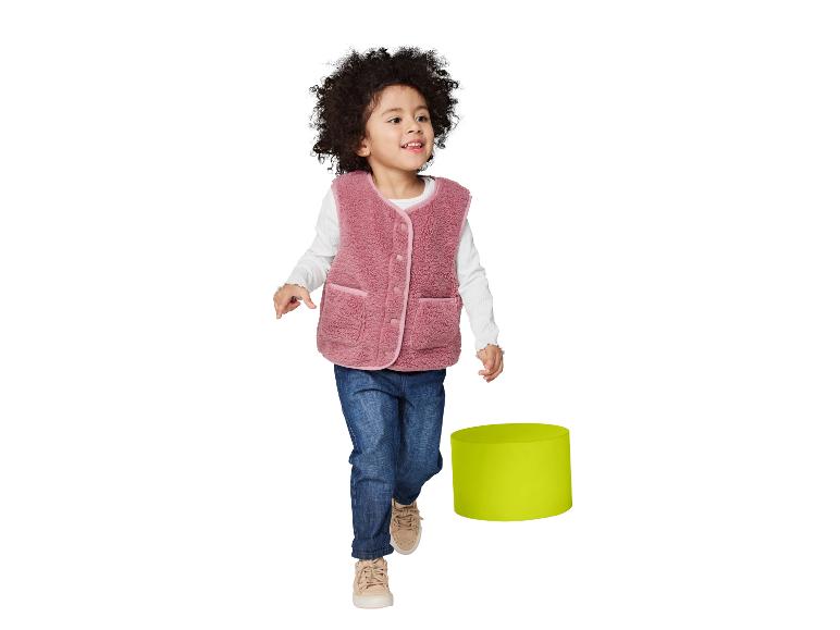 Enfant en gilet rose et jean, souriant et regardant sur le côté.