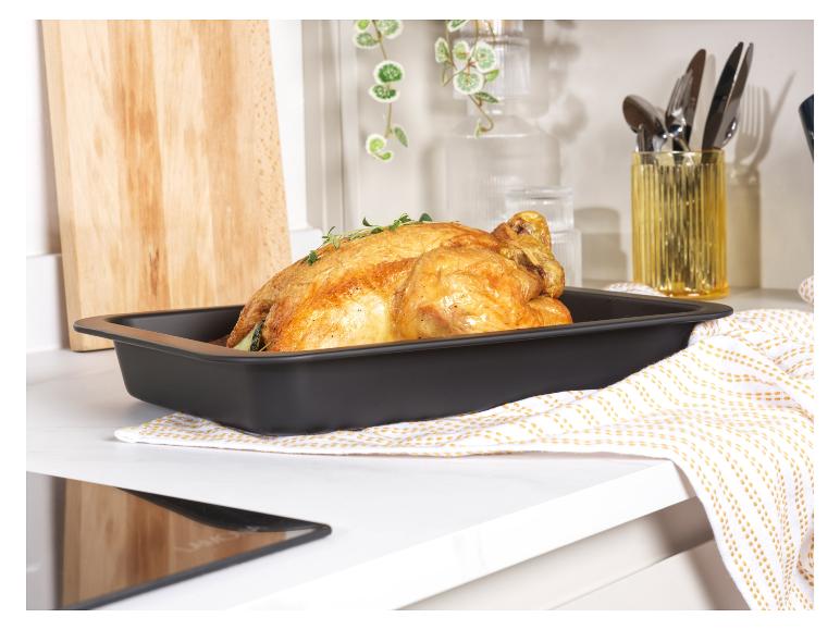 Un poulet rôti dans un plat à four noir sur un comptoir blanc.