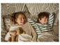 Deux enfants riant au lit, vêtus de pyjamas avec une couette à motifs.