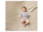Un bébé allongé sur une couverture beige, portant un body gris avec un ours imprimé.