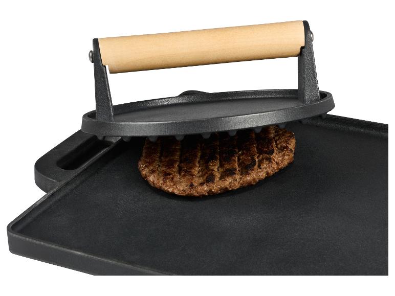 Grill en fonte avec un burger et une presse sur fond blanc.