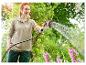 Une femme arrose des fleurs avec un tuyau d'arrosage Gardena.
