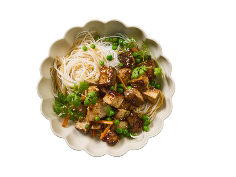 Plat de tofu et nouilles avec petits pois, carottes et coriandre dans un bol festonné.
