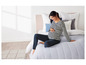 Une femme enceinte en pyjama rayé et pantalon bleu assise sur un lit.