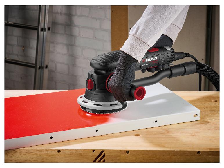 Ponceuse manuelle ponçant une surface rouge sur une table en bois.