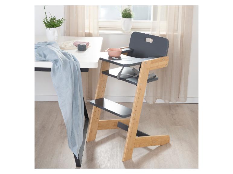 Chaise haute en bois et grise avec bol rose et cuillère, à côté d'une table blanche.