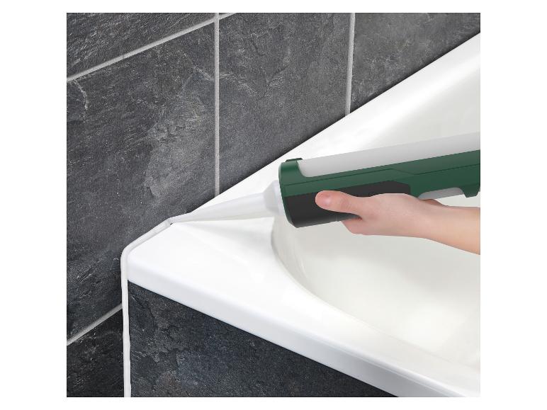 Main appliquant du mastic sur le bord d'une baignoire blanche contre des carreaux gris foncé