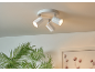 Spot de plafond blanc avec trois lumières orientables, au-dessus d'une plante et d'un tableau.