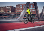 Homme en veste de cyclisme jaune et casque noir sur un vélo électrique sur un pont.