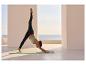 Femme faisant du yoga en extérieur avec vue sur la mer, portant un legging noir et un top de sport vert menthe.