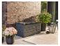 Coffre de rangement de jardin gris foncé sur une terrasse avec plantes en pot et tapis.