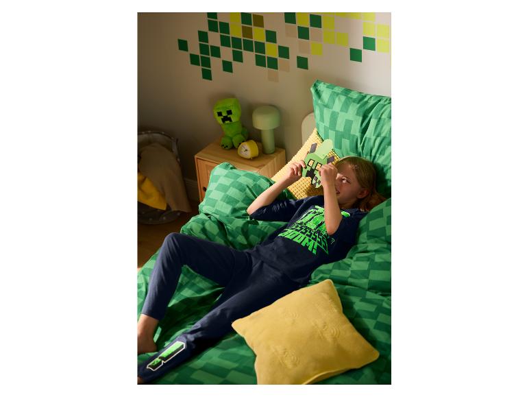 Enfant en pyjama Minecraft, allongé sur un lit avec literie assortie et décor thématique.