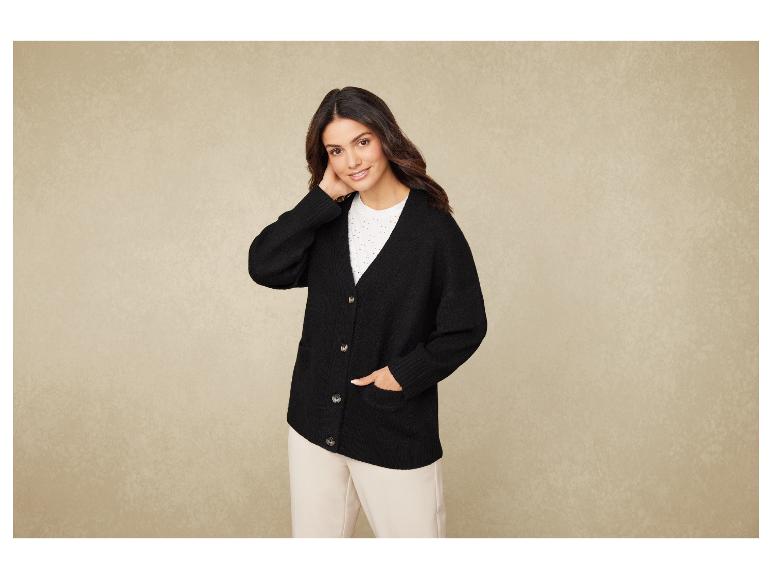 Une femme porte un pull noir et un pantalon beige.