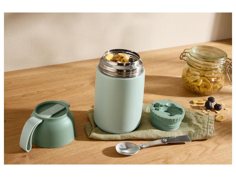 Thermos alimentaire avec petit-déjeuner, bol, cuillère et pot de bananes séchées sur table en bois.