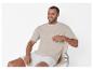 Homme portant un t-shirt beige et un short blanc, assis sur une chaise.