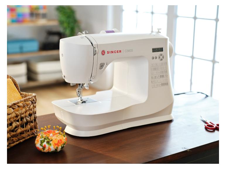 Machine à coudre Singer blanche sur une table en bois, avec un panier de fournitures et un coussin à épingles.
