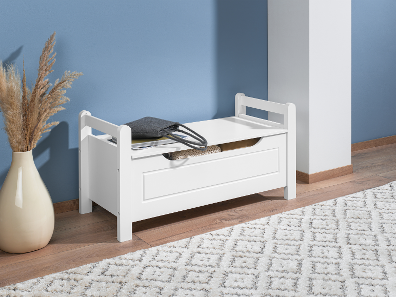 Banc de rangement en bois blanc avec couvercle à charnières sur un tapis dans une pièce.