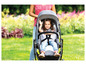 Un enfant dans une poussette grise dans un jardin vert.