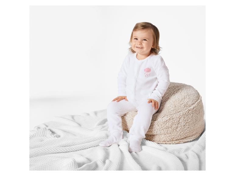 Un bébé assis sur un coussin en peluche, porte un pyjama blanc avec un motif nuage.