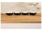 Quatre bols noirs sur une table en bois clair, avec des ombres de feuilles sur le mur.
