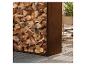 Pile de bois de chauffage dans un support métallique à côté d'une plante en pot sur un plancher en bois.