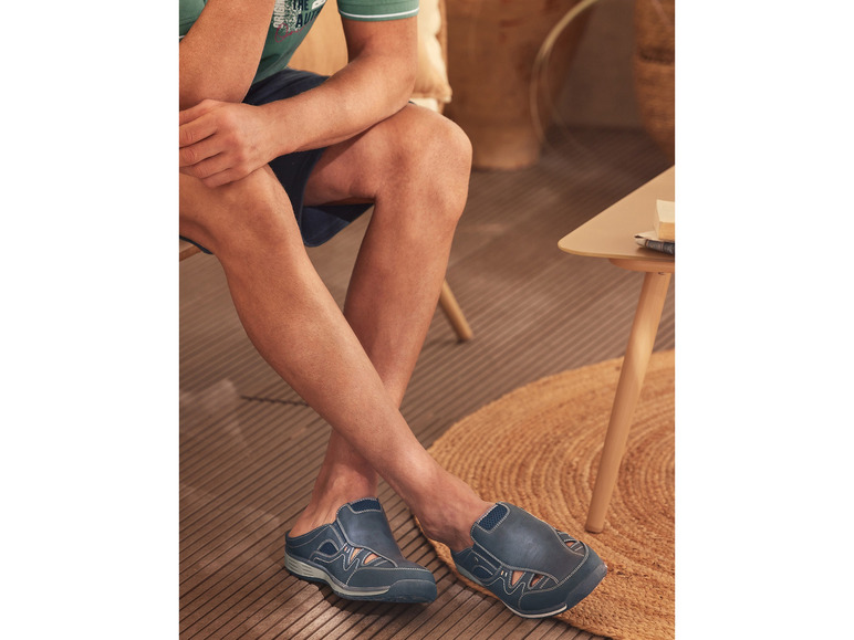 Un homme porte des sandales bleues sur un sol en bois.
