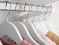 Cintres blancs avec des vêtements roses et bruns dans une armoire.
