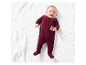 Bébé souriant dans une grenouillère bordeaux sur une couverture blanche.