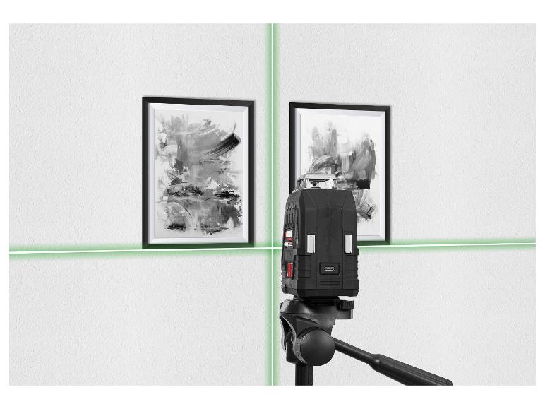 Un niveau laser projette des lignes vertes sur un mur blanc avec deux tableaux abstraits encadrés.
