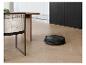 Robot aspirateur noir nettoyant un parquet en chevrons dans une cuisine moderne.