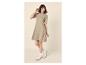 Femme souriante en robe beige à manches courtes et baskets blanches.