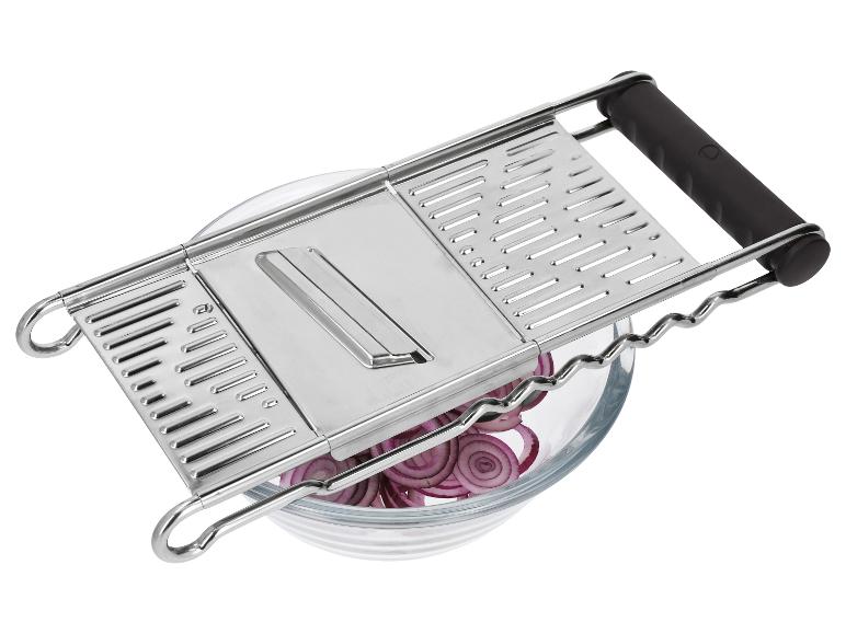 Mandoline de cuisine en métal avec poignées noires sur un bol en verre avec des oignons rouges tranchés.
