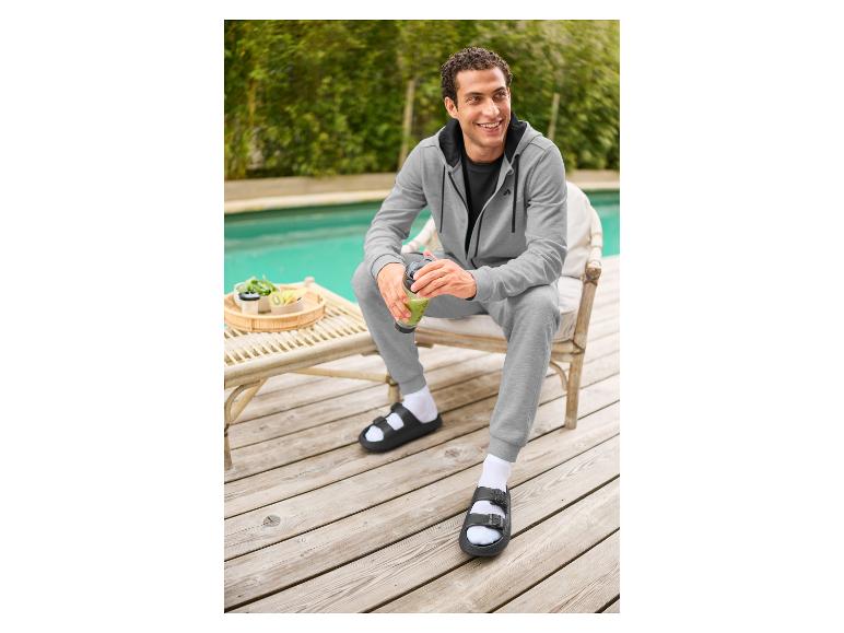 Homme en jogging gris et mules noires CRIVIT au bord de la piscine.