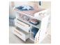 Table à langer blanche avec tiroirs et étagères, décorée d'accessoires et de jouets pour bébé.
