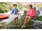 Femme et enfant en camping avec une table pliante, des chaises de camping et des tentes.