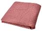Jeté de lit matelassé rose avec motif géométrique.