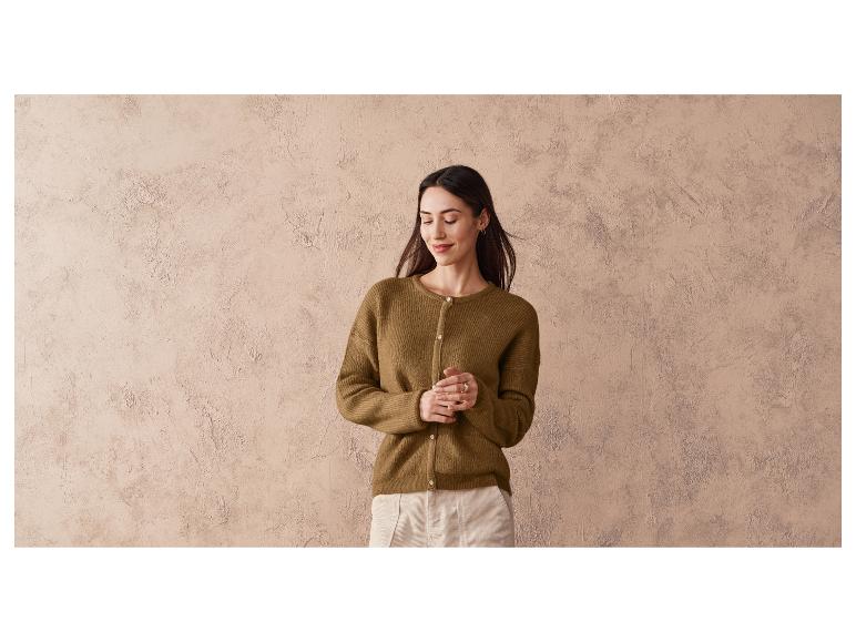 Une femme porte un pull marron et un pantalon blanc.